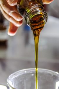 person holding clear bottle pouring olive oil